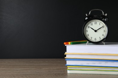Photo of Alarm clock and stacked books on wooden table near blackboard, space for text. School time
