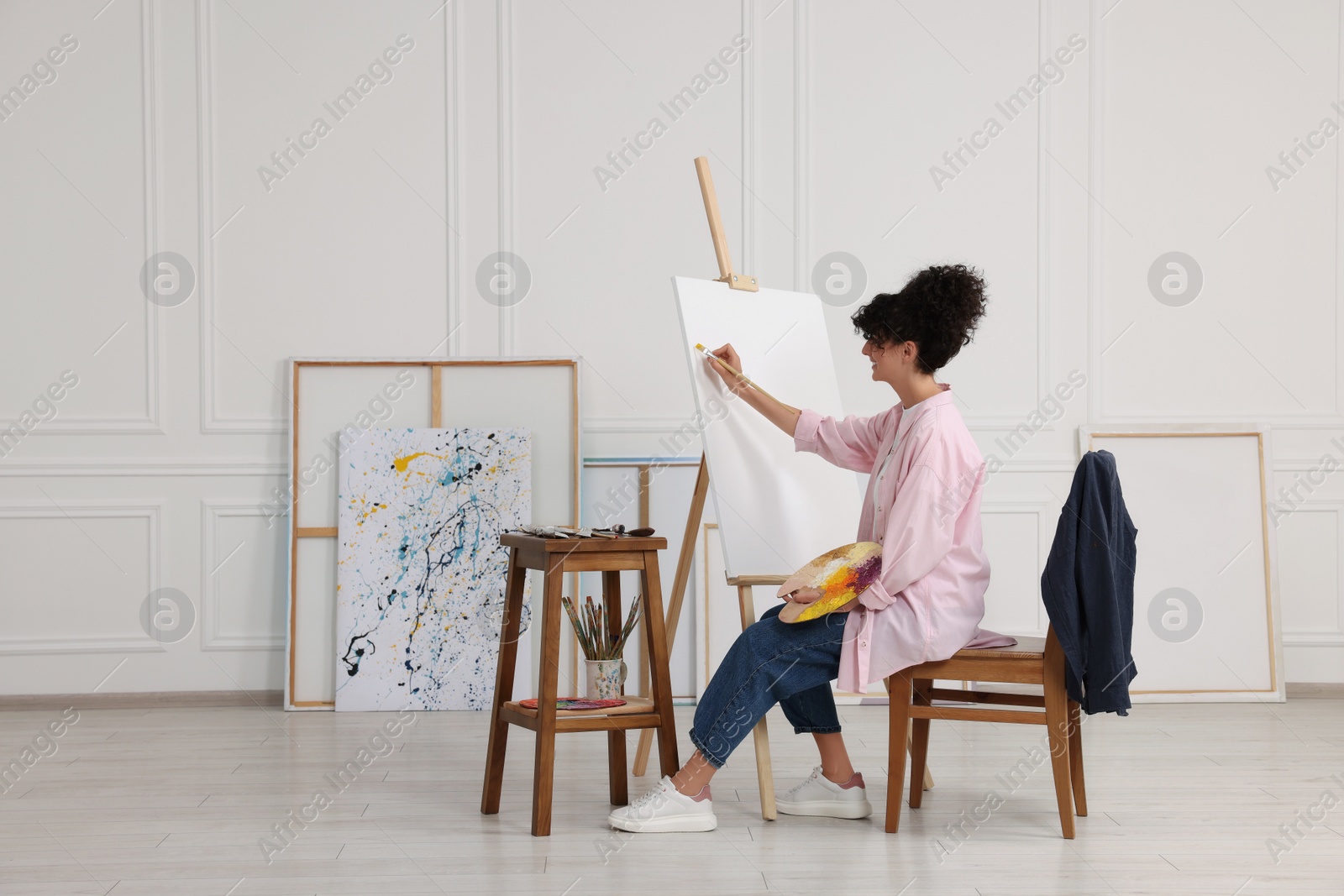 Photo of Young woman painting on easel with canvas in studio