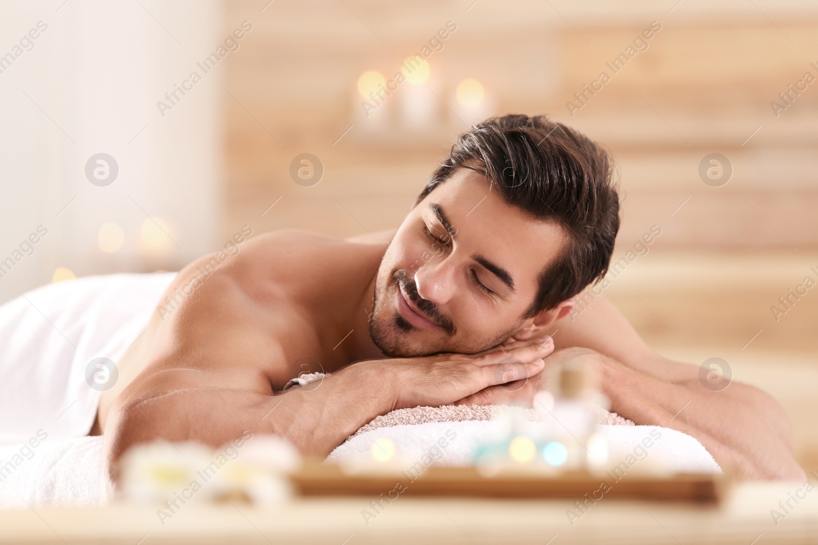 Photo of Handsome young man relaxing on massage table in spa salon