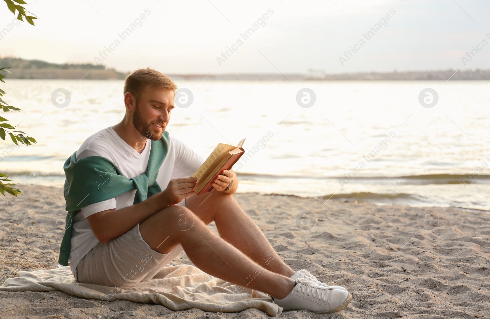 Photo of Young man reading book on sandy beach near sea