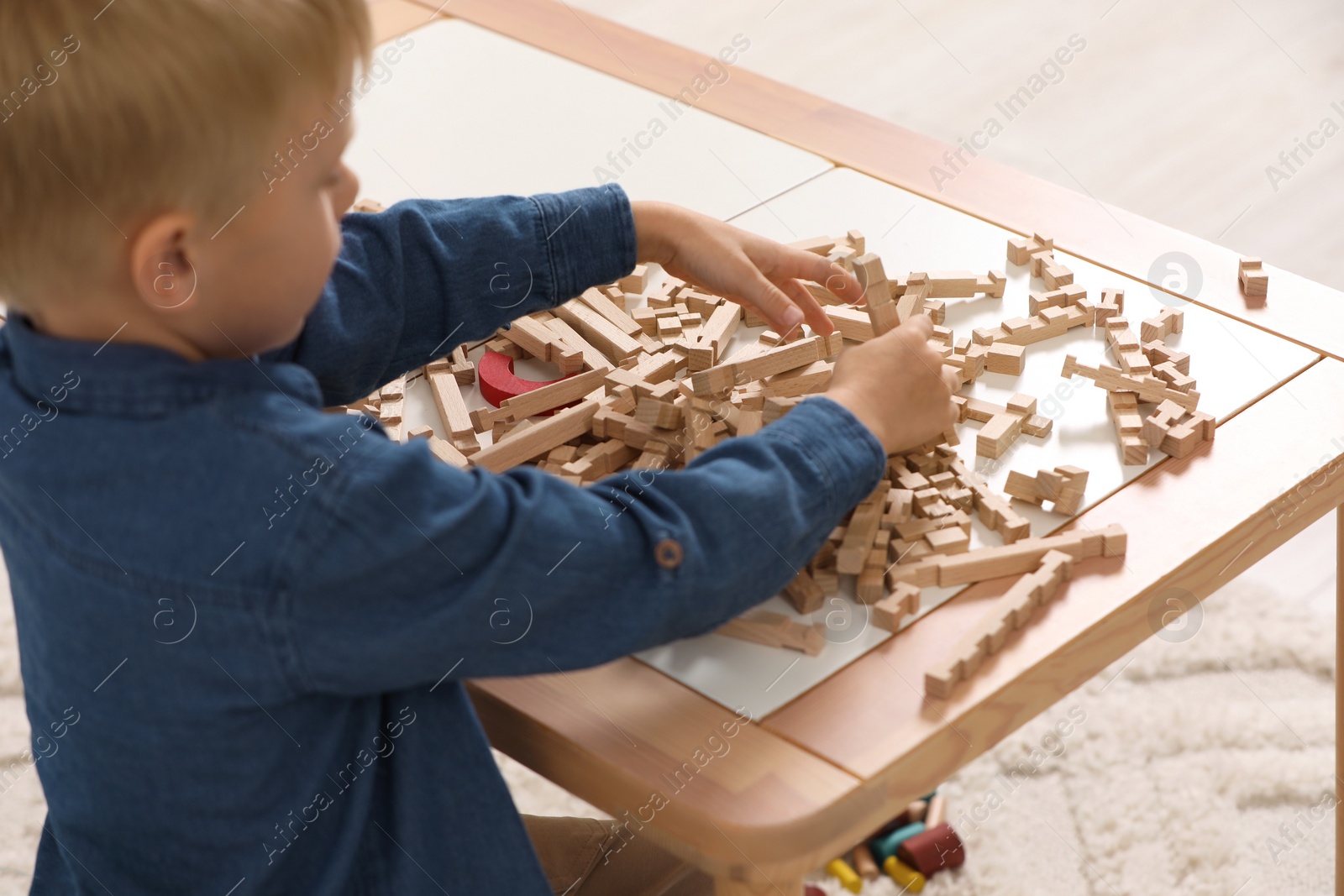 Photo of Little boy playing with wooden blocks at table indoors. Child's toy