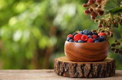 Different fresh berries in bowl on wooden table outdoors. Space for text