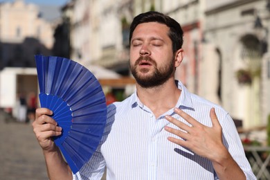 Man with hand fan suffering from heat outdoors