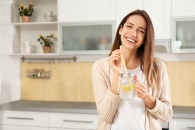 Photo of Young woman with mason jar of lemon water in kitchen