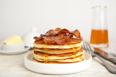 Delicious pancakes with maple syrup and fried bacon on white wooden table