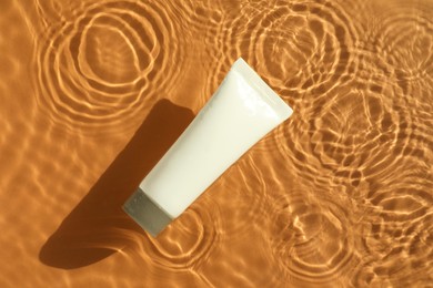 Tube with moisturizing cream in water on orange background, top view