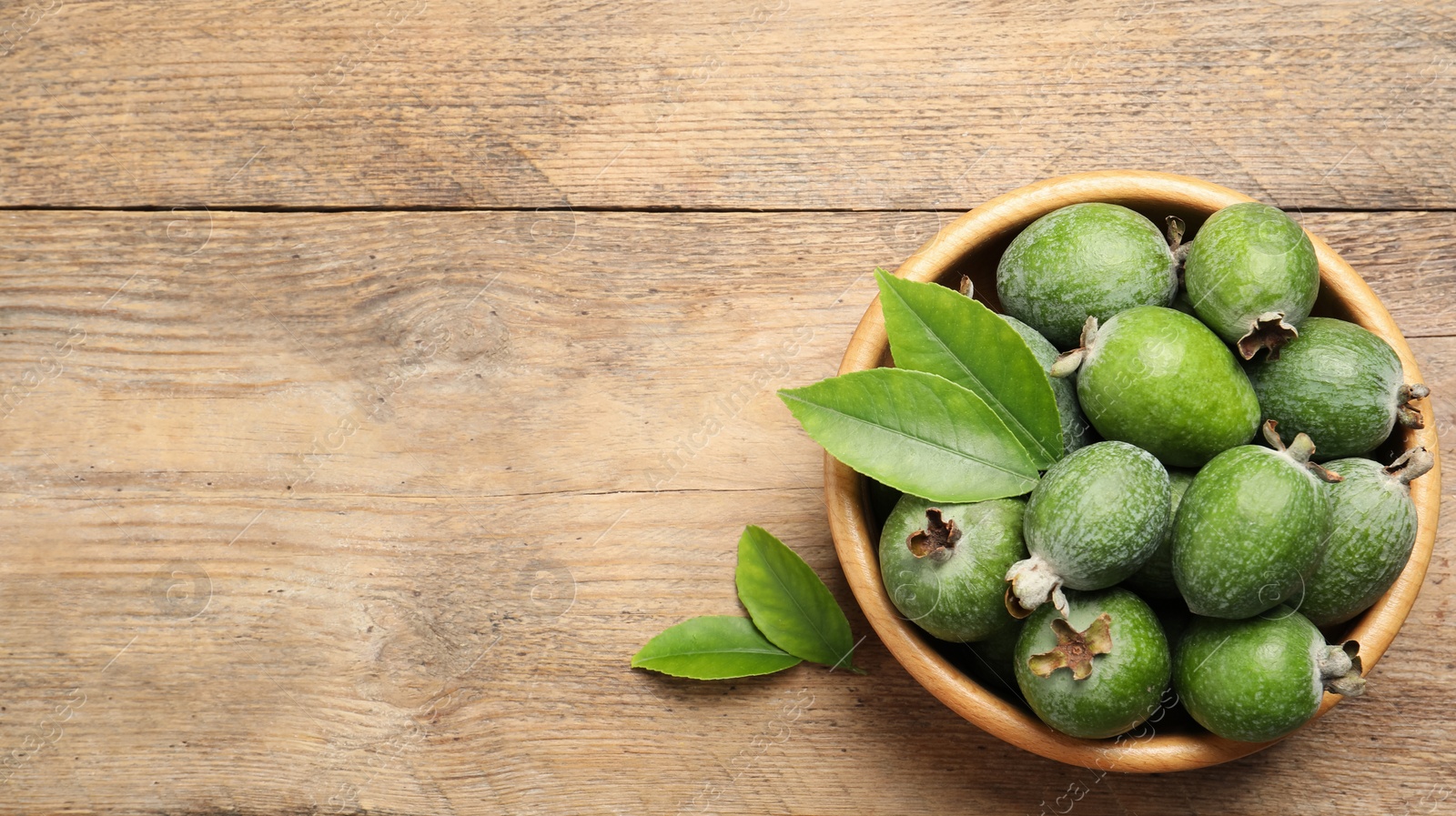 Image of Fresh green feijoa fruits in bowl on wooden table, top view with space for text. Banner design