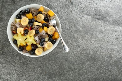 Delicious exotic fruit salad on grey table, top view. Space for text