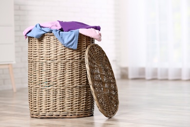 Wicker laundry basket with dirty clothes on floor indoors. Space for text