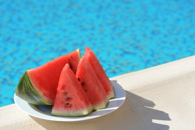 Photo of Slices of watermelon on white plate near swimming pool outdoors. Space for text