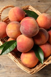 Photo of Fresh peaches and leaves in basket on wooden table, top view