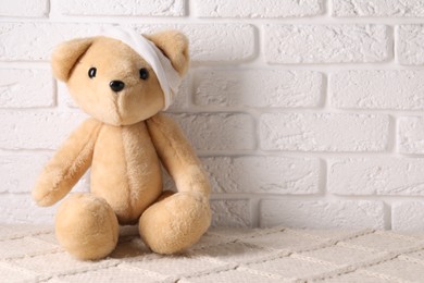Photo of Toy bear with bandage on soft surface near white brick wall, space for text