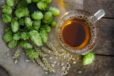 Photo of Mug with beer, fresh hops and ears of wheat on wooden table, top view