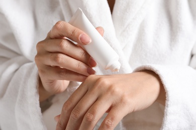 Photo of Woman in bathrobe applying moisturizing hand cream, closeup. Winter skin care cosmetic