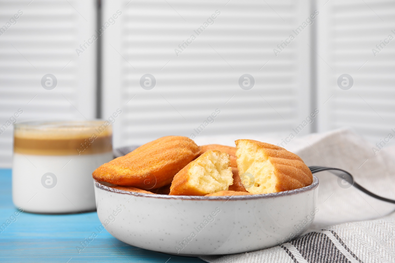 Photo of Tasty madeleine cookies in bowl on light blue wooden table