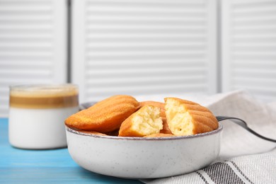 Photo of Tasty madeleine cookies in bowl on light blue wooden table