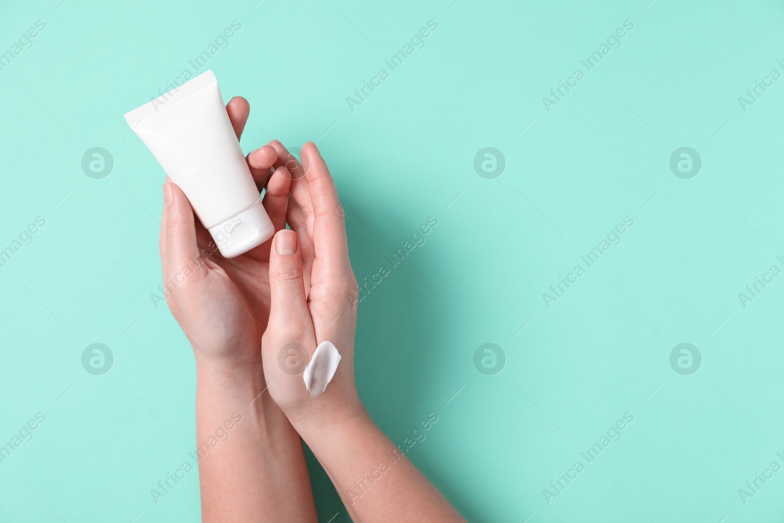 Photo of Woman with tube of hand cream on turquoise background, top view. Space for text