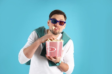 Photo of Man with 3D glasses eating tasty popcorn on color background