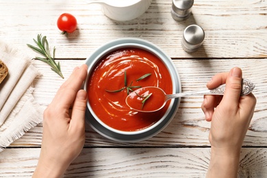 Woman eating fresh homemade tomato soup at wooden table, top view