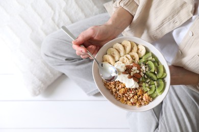 Woman eating tasty granola indoors, top view
