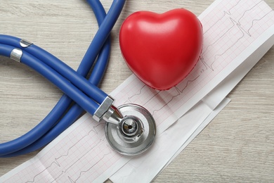 Photo of Cardiogram report, red heart and stethoscope on wooden table, flat lay