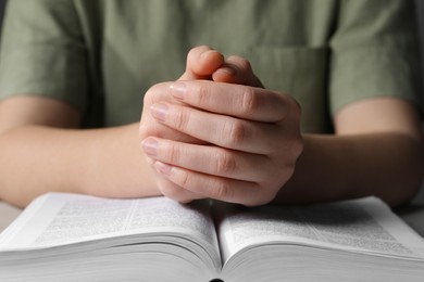 Photo of Woman holding hands clasped while praying over Bible at table, closeup