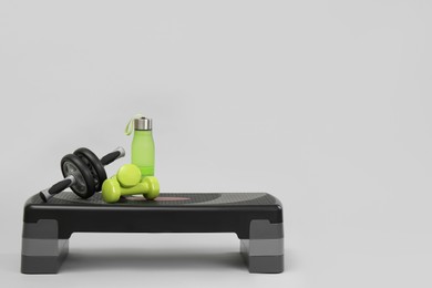 Photo of Step platform, water bottle, dumbbells and abdominal wheel on light background, space for text. Sport equipment