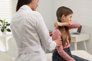 Photo of Doctor examining coughing girl in hospital. Cold symptoms