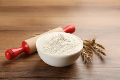 Photo of Bowl of flour, wheat ears and rolling pin on wooden table. Space for text