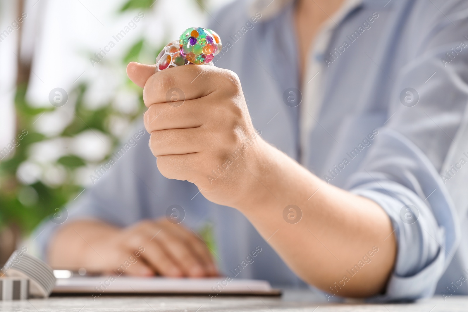 Photo of Woman squeezing colorful slime in office, closeup. Antistress toy