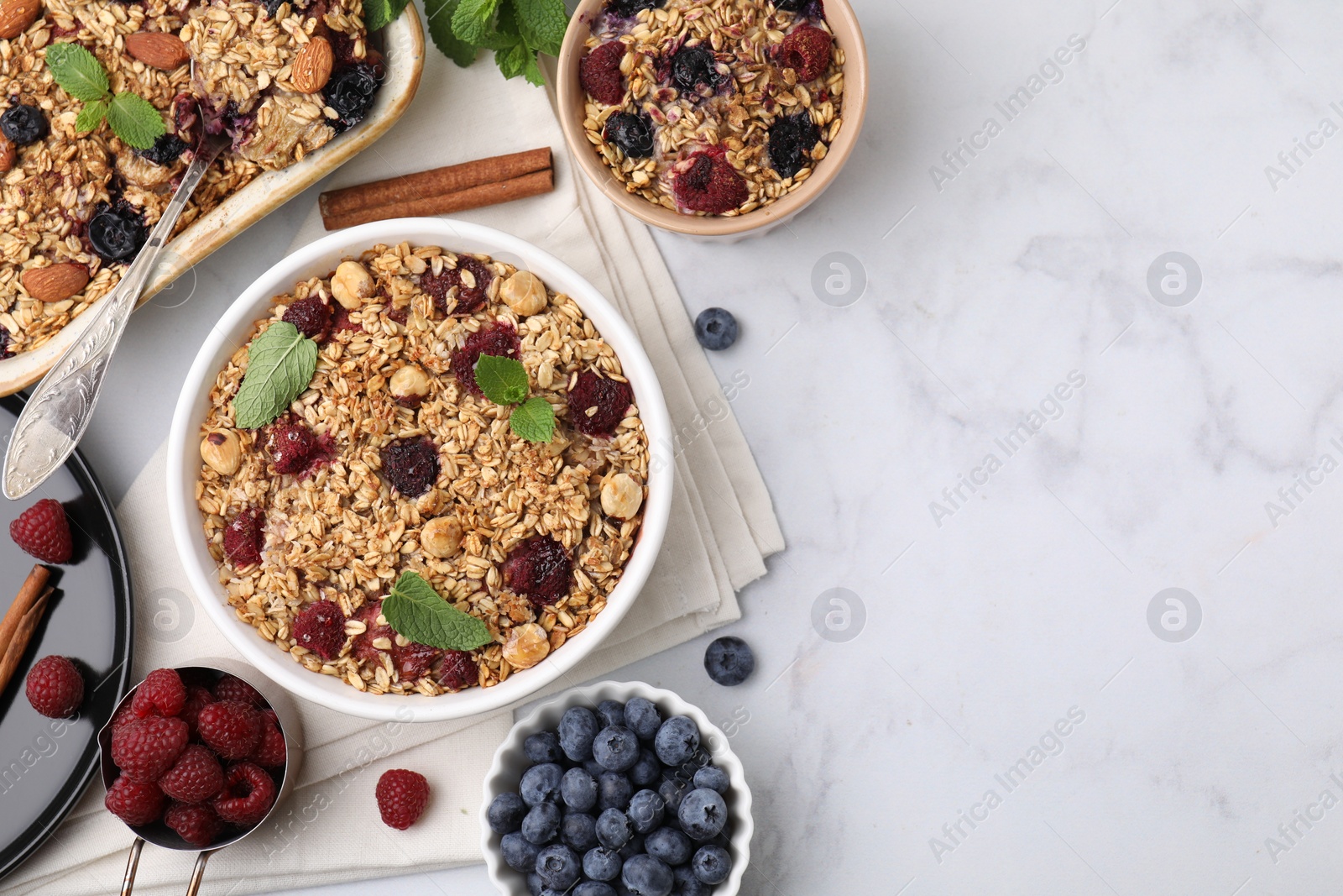 Photo of Tasty baked oatmeal with berries, nuts and cinnamon sticks on white table, flat lay. Space for text