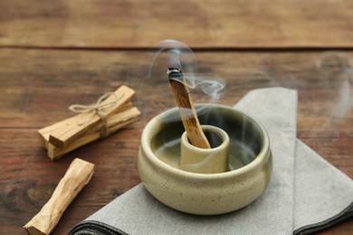 Palo Santo stick smoldering in holder on wooden table