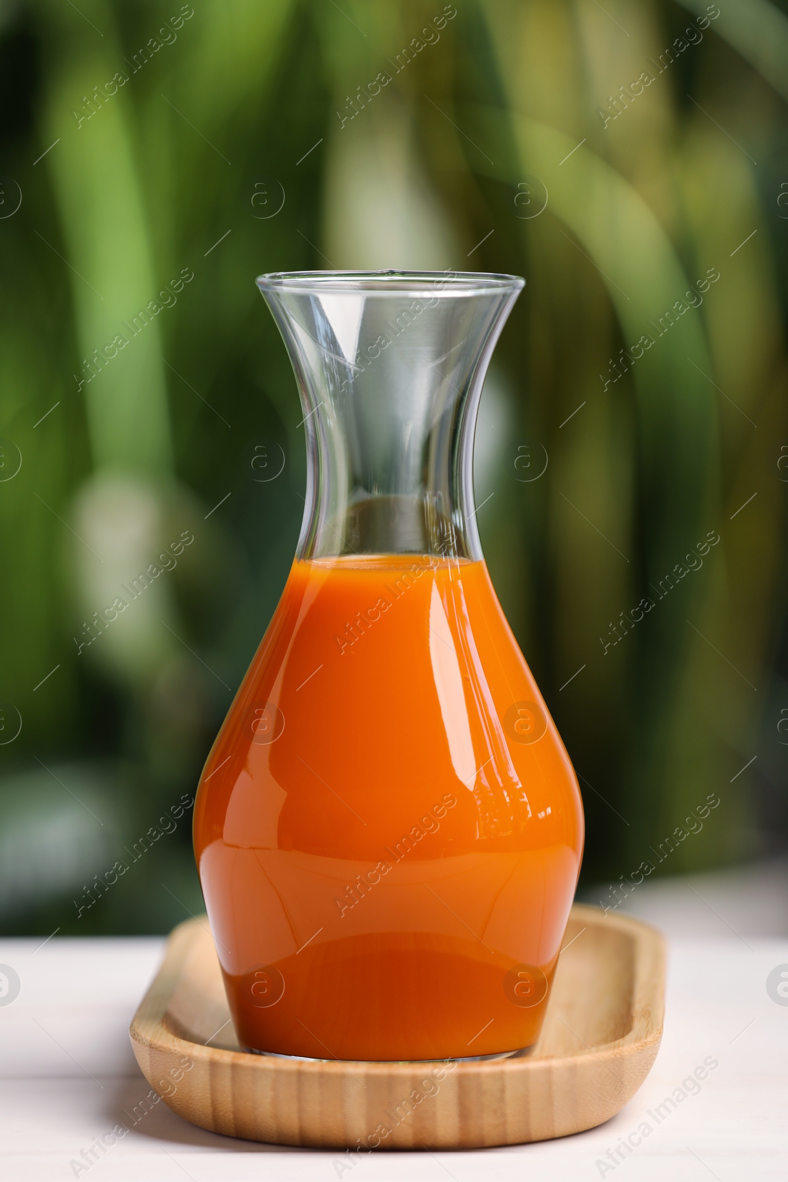 Photo of Tasty carrot juice on white table outdoors, closeup