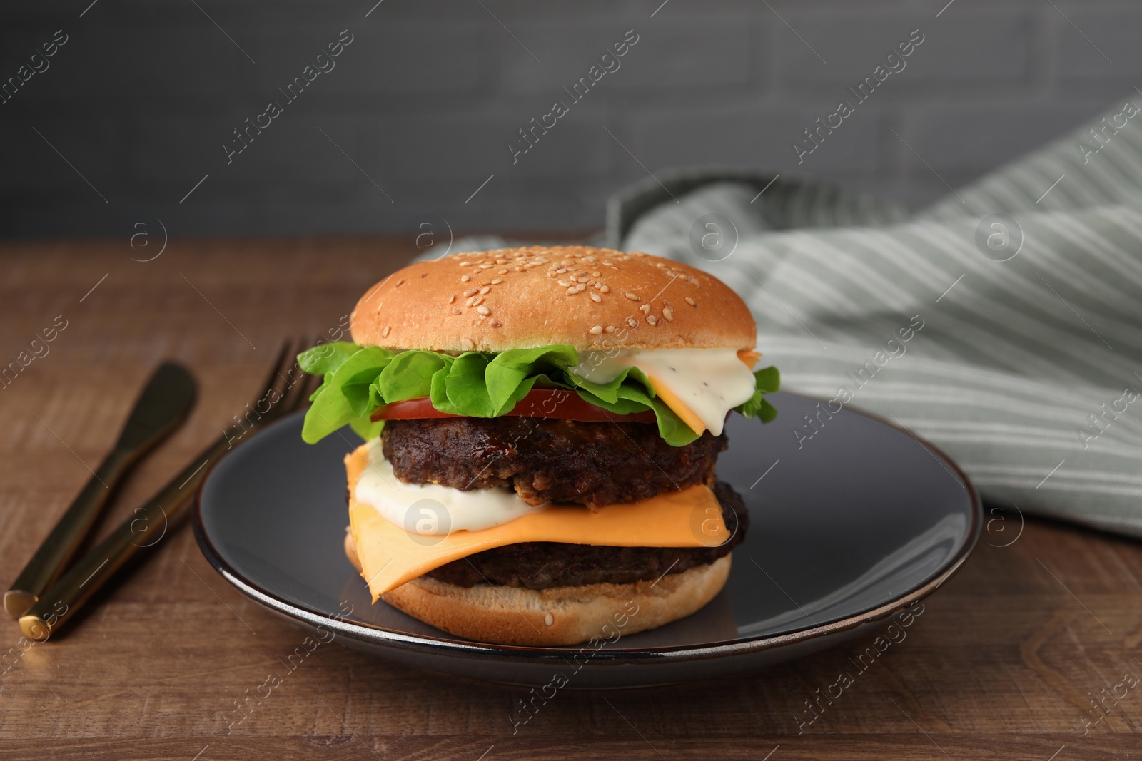 Photo of Tasty cheeseburger with patties and cutlery on wooden table