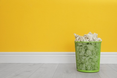 Photo of Metal bin with crumpled paper against color wall, space for text