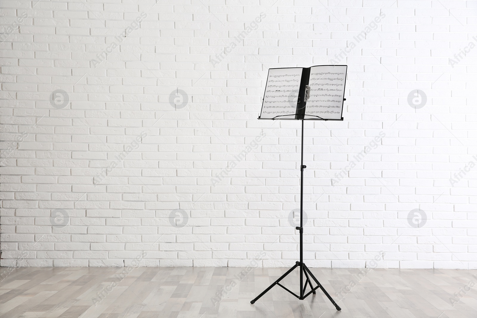 Photo of Note stand with music sheets near brick wall indoors. Space for text