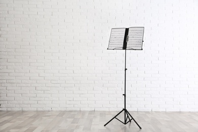 Note stand with music sheets near brick wall indoors. Space for text