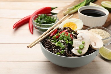 Photo of Tasty buckwheat noodles (soba) with mushrooms, onion, chili pepper, egg and chopsticks on wooden table, space for text