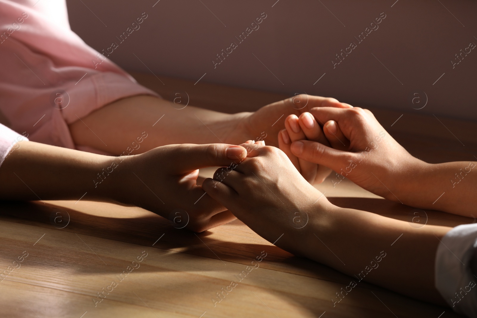 Photo of Religious women holding hands and praying together at wooden table, closeup