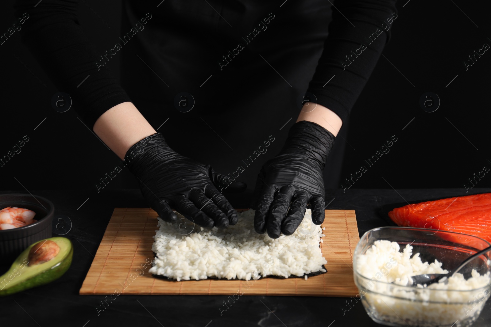 Photo of Chef in gloves making sushi roll at dark table, closeup