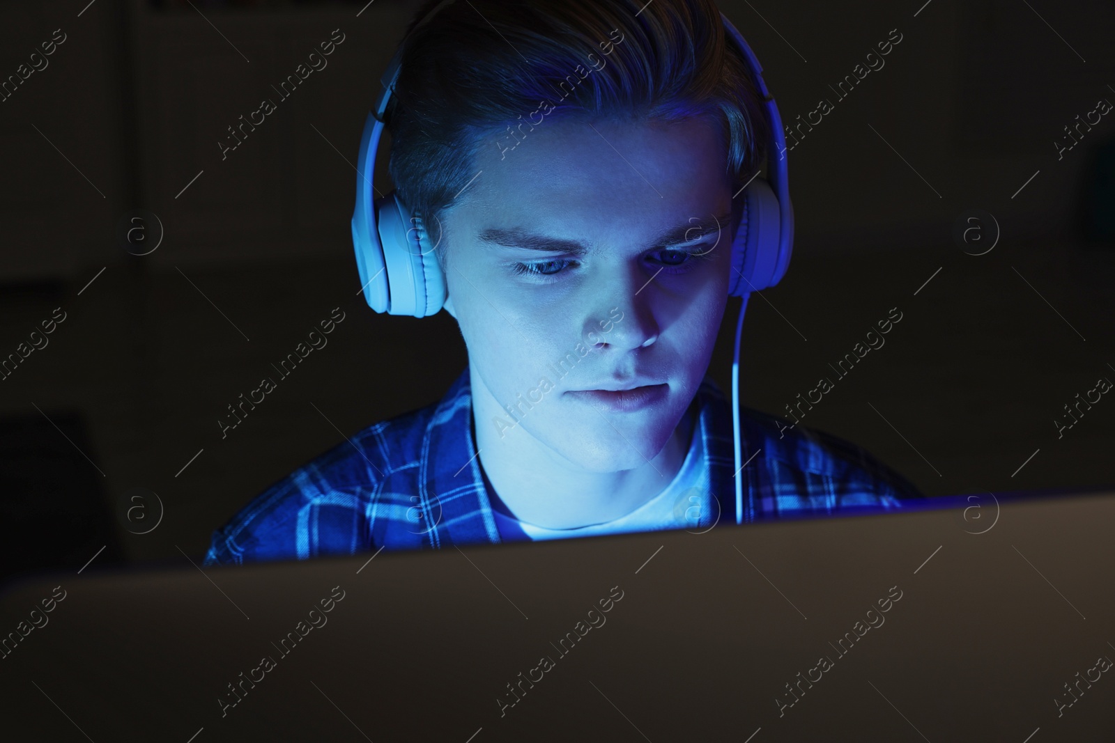 Photo of Teenage boy in headphones using computer at night. Internet addiction