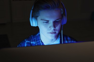 Photo of Teenage boy in headphones using computer at night. Internet addiction