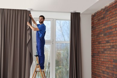 Photo of Worker in uniform hanging window curtain indoors