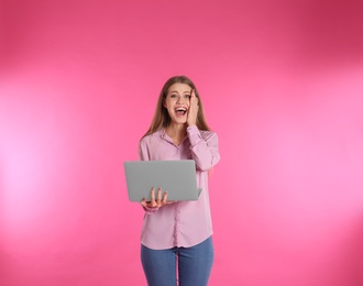 Emotional young woman with laptop celebrating victory on color background