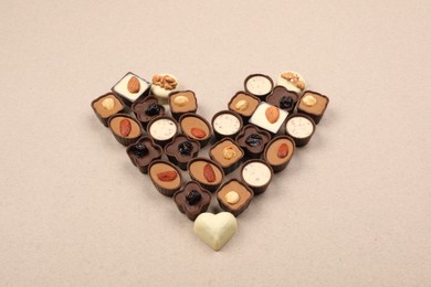 Heart made with delicious chocolate candies on beige background, above view