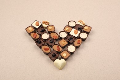 Photo of Heart made with delicious chocolate candies on beige background, above view