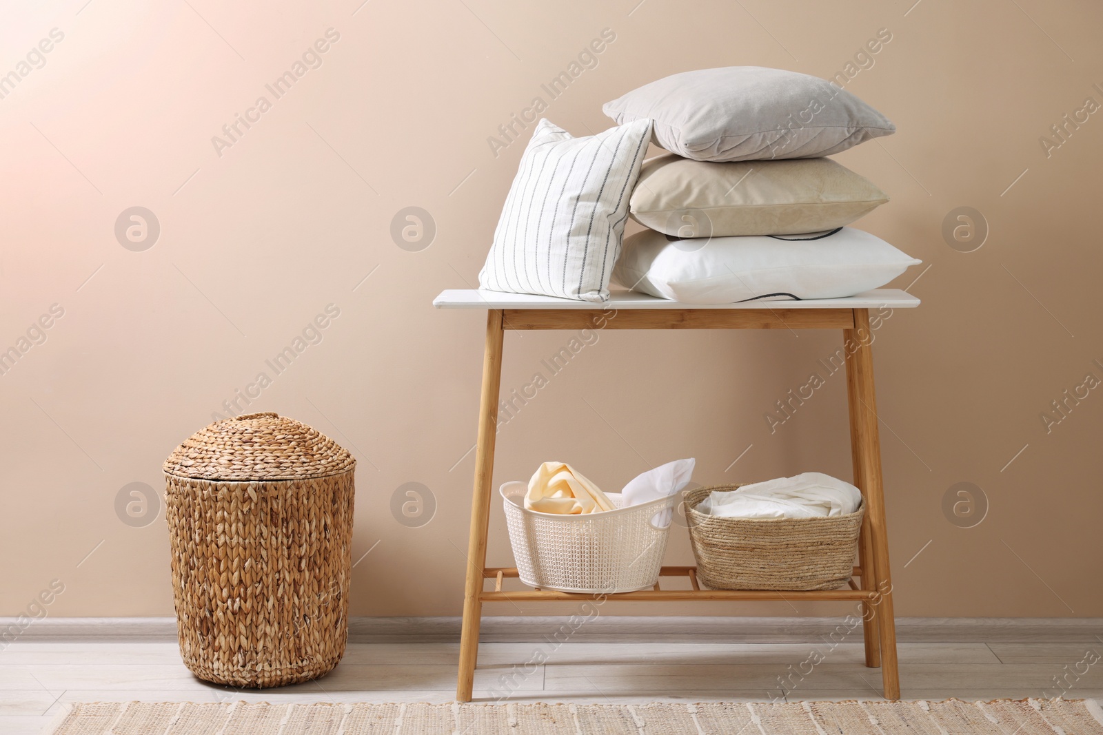 Photo of Soft pillows and laundry baskets near beige wall indoors