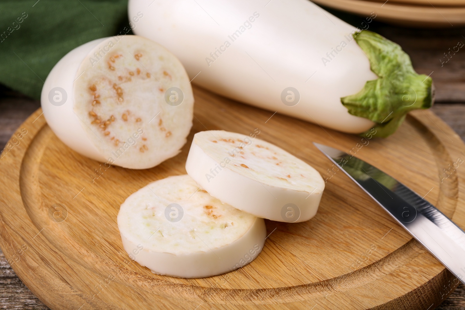 Photo of Raw eggplants and knife on wooden board, closeup