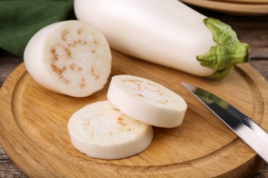 Raw eggplants and knife on wooden board, closeup