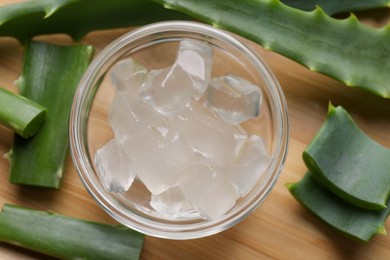 Aloe vera gel and slices of plant on wooden table, flat lay